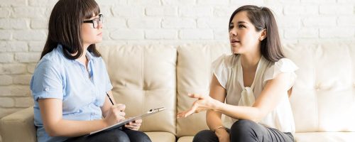 Pretty young woman talking to female therapist on sofa, sharing her issues during psychotherapy.
